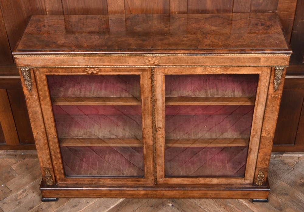 A Victorian burr walnut low cabinet featuring two glazed doors, intricate boxwood inlay, and ornate bronzed corner mounts. View X