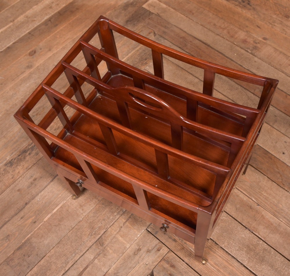 An Edwardian mahogany Canterbury featuring four slatted compartments, an integrated carrying handle, a lower drawer with brass knobs, and square tapered legs on brass castors. View II