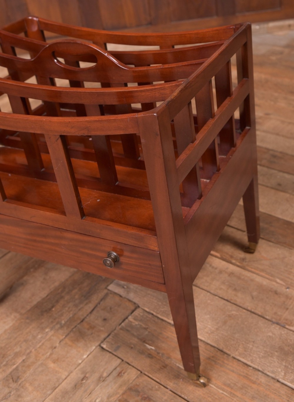 An Edwardian mahogany Canterbury featuring four slatted compartments, an integrated carrying handle, a lower drawer with brass knobs, and square tapered legs on brass castors. View III