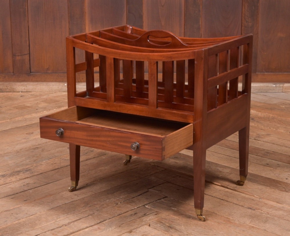 An Edwardian mahogany Canterbury featuring four slatted compartments, an integrated carrying handle, a lower drawer with brass knobs, and square tapered legs on brass castors. View IV
