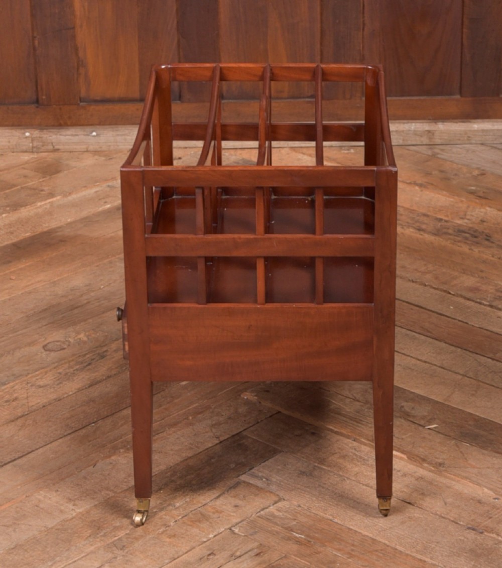 An Edwardian mahogany Canterbury featuring four slatted compartments, an integrated carrying handle, a lower drawer with brass knobs, and square tapered legs on brass castors. View V