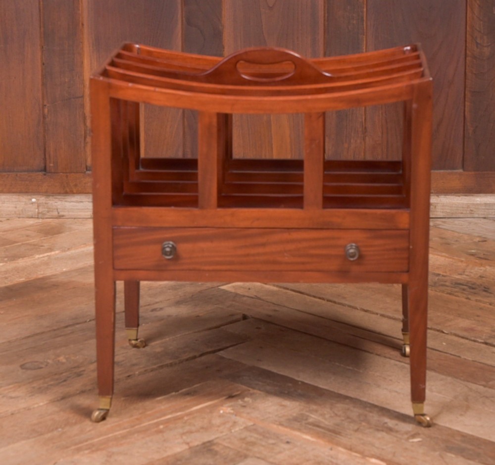 An Edwardian mahogany Canterbury featuring four slatted compartments, an integrated carrying handle, a lower drawer with brass knobs, and square tapered legs on brass castors. View VII