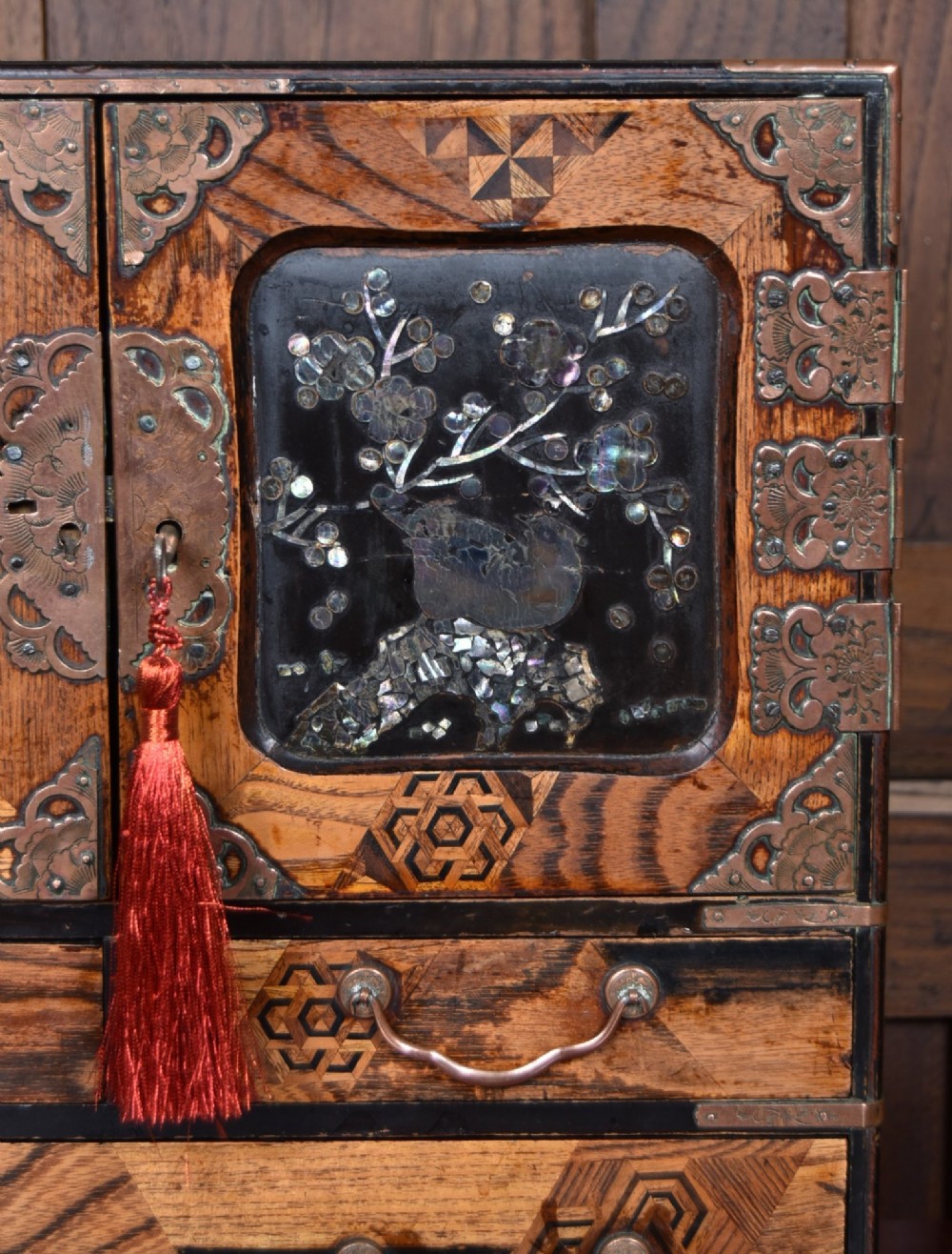 A Japanese tabletop wooden kodansu cabinet featuring geometric marquetry, mother-of-pearl shell inlay on dark lacquered door panels, metal mounts, and lower drawers. View II