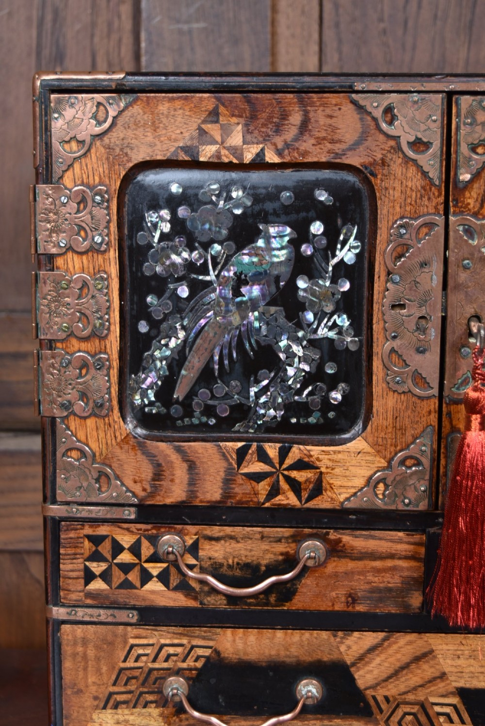 A Japanese tabletop wooden kodansu cabinet featuring geometric marquetry, mother-of-pearl shell inlay on dark lacquered door panels, metal mounts, and lower drawers. View III