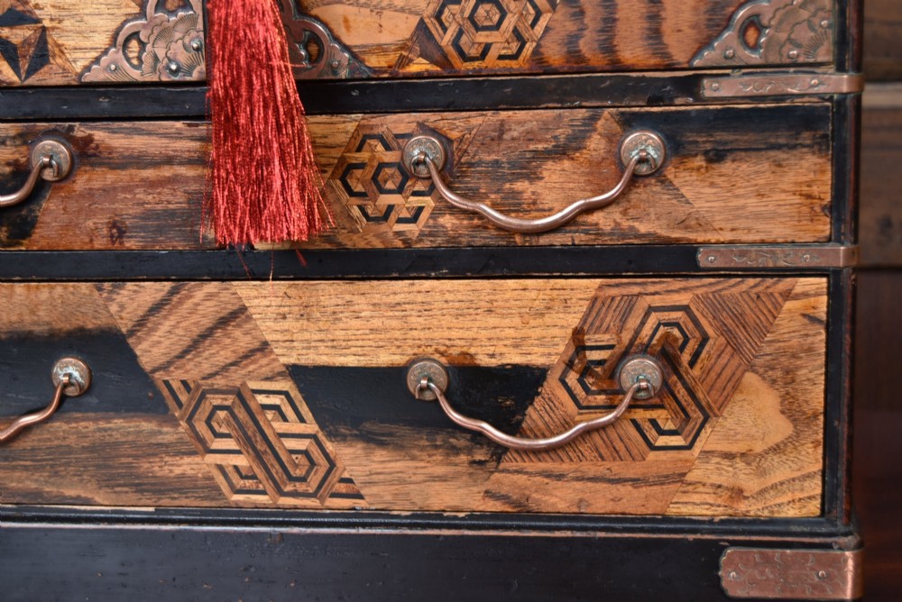 A Japanese tabletop wooden kodansu cabinet featuring geometric marquetry, mother-of-pearl shell inlay on dark lacquered door panels, metal mounts, and lower drawers. View IV
