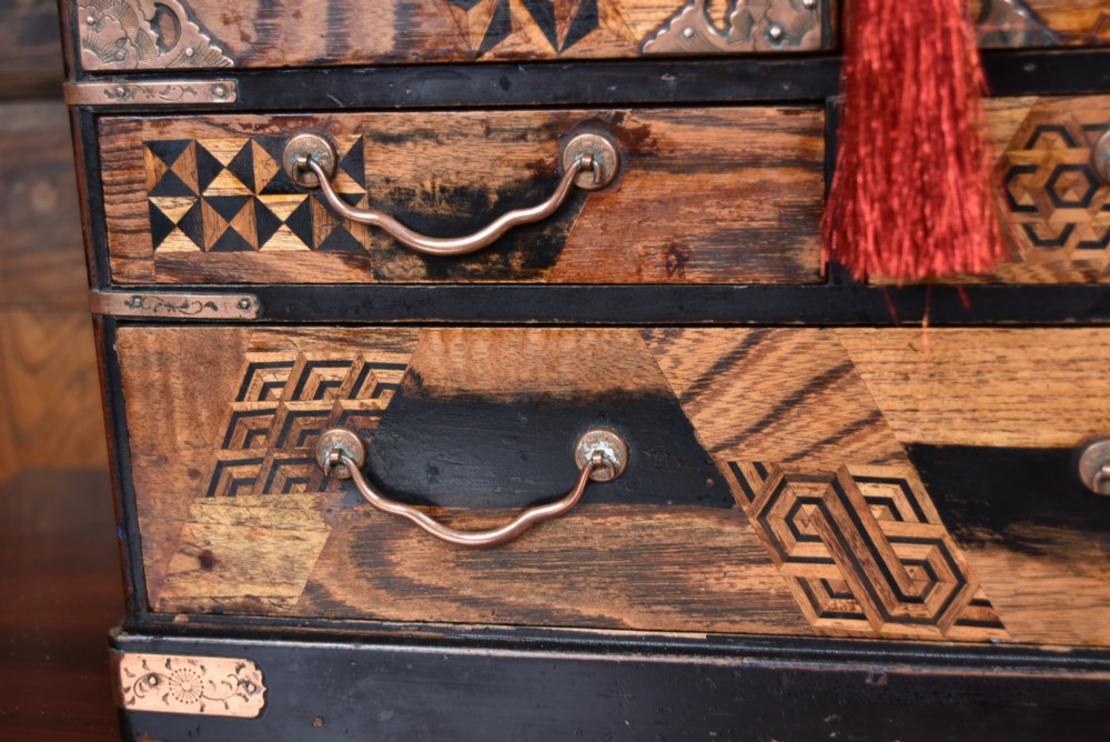 A Japanese tabletop wooden kodansu cabinet featuring geometric marquetry, mother-of-pearl shell inlay on dark lacquered door panels, metal mounts, and lower drawers. View V