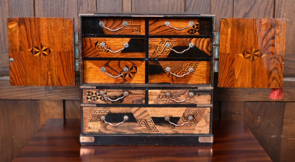 A Japanese tabletop wooden kodansu cabinet featuring geometric marquetry, mother-of-pearl shell inlay on dark lacquered door panels, metal mounts, and lower drawers. View VI
