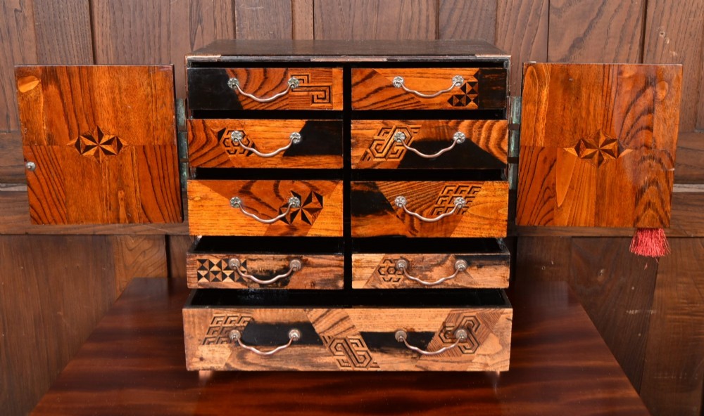 A Japanese tabletop wooden kodansu cabinet featuring geometric marquetry, mother-of-pearl shell inlay on dark lacquered door panels, metal mounts, and lower drawers. View VII