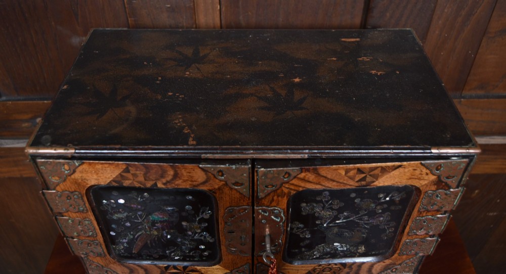 A Japanese tabletop wooden kodansu cabinet featuring geometric marquetry, mother-of-pearl shell inlay on dark lacquered door panels, metal mounts, and lower drawers. View XI
