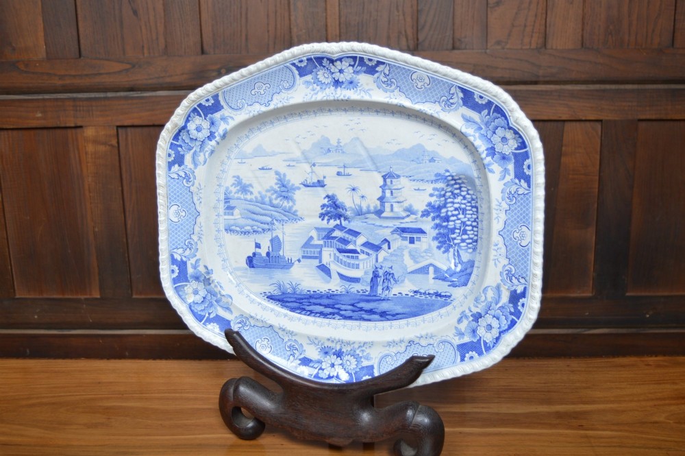 An oval blue and white earthenware transferware platter featuring an oriental landscape scene surrounded by a moulded floral pattern border. View III