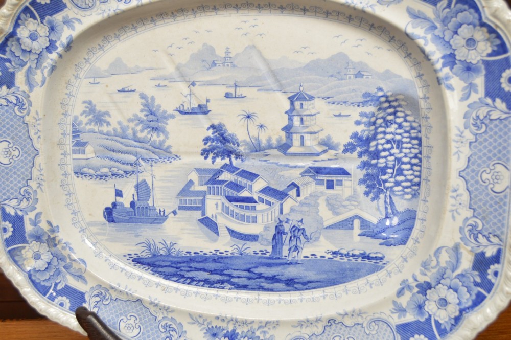 An oval blue and white earthenware transferware platter featuring an oriental landscape scene surrounded by a moulded floral pattern border. View V