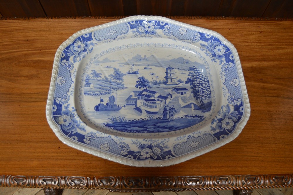 An oval blue and white earthenware transferware platter featuring an oriental landscape scene surrounded by a moulded floral pattern border. View VI