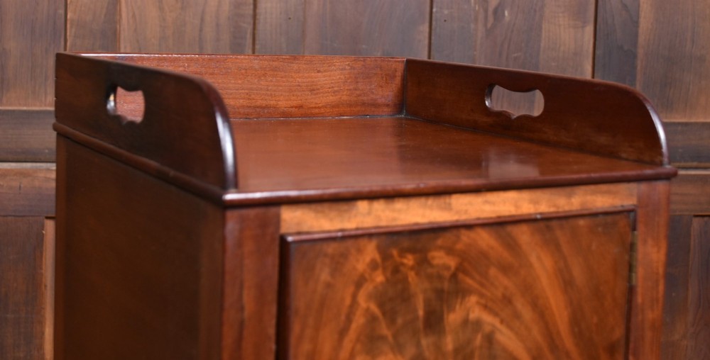 An antique Georgian flame mahogany tray-top pot cupboard featuring tall turned legs, a single cabinet door with a brass knob, and cut-out handles in the gallery top. View II