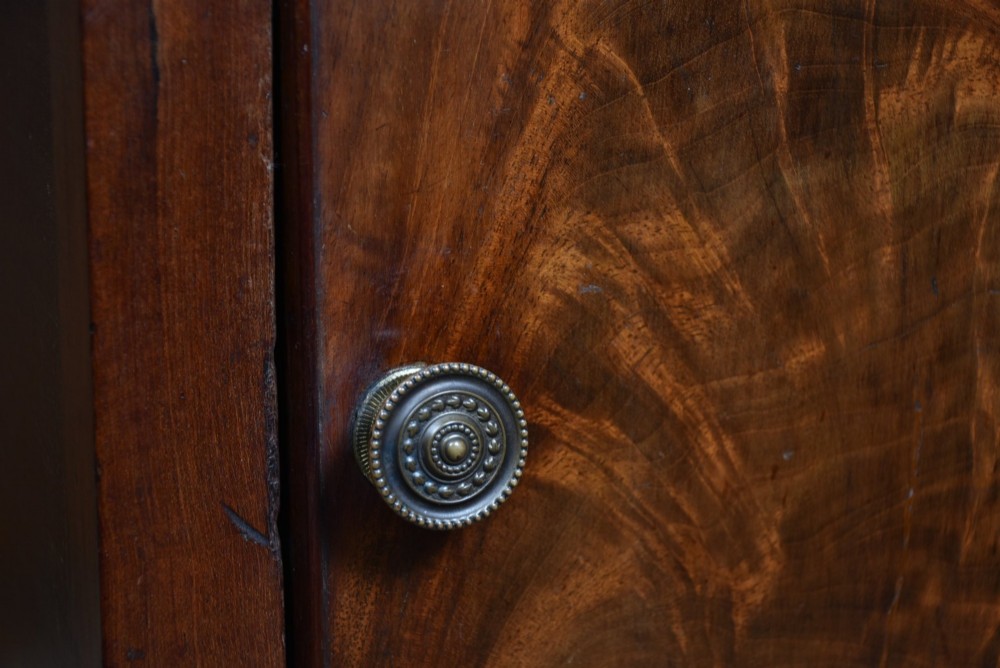An antique Georgian flame mahogany tray-top pot cupboard featuring tall turned legs, a single cabinet door with a brass knob, and cut-out handles in the gallery top. View III
