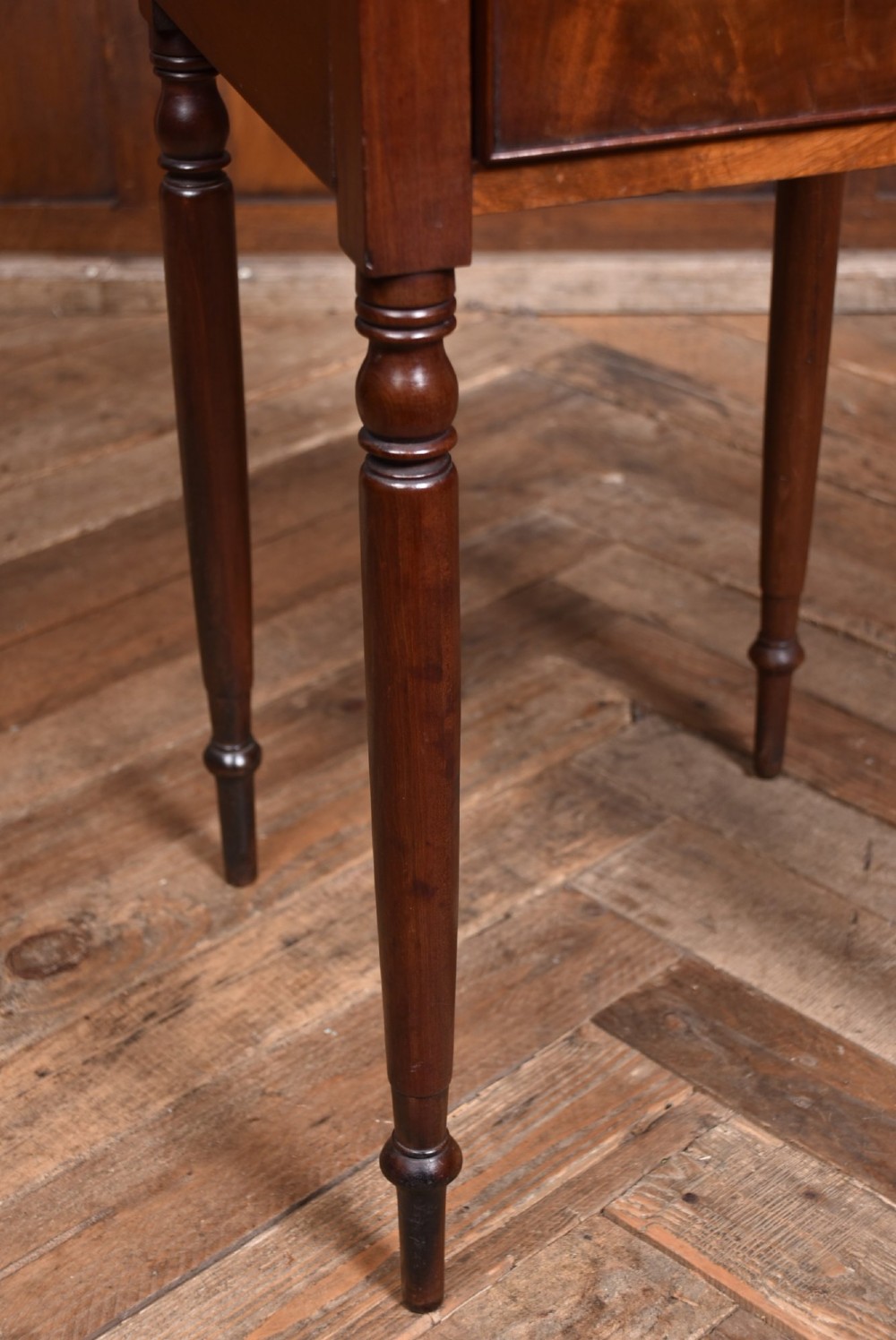 An antique Georgian flame mahogany tray-top pot cupboard featuring tall turned legs, a single cabinet door with a brass knob, and cut-out handles in the gallery top. View IV
