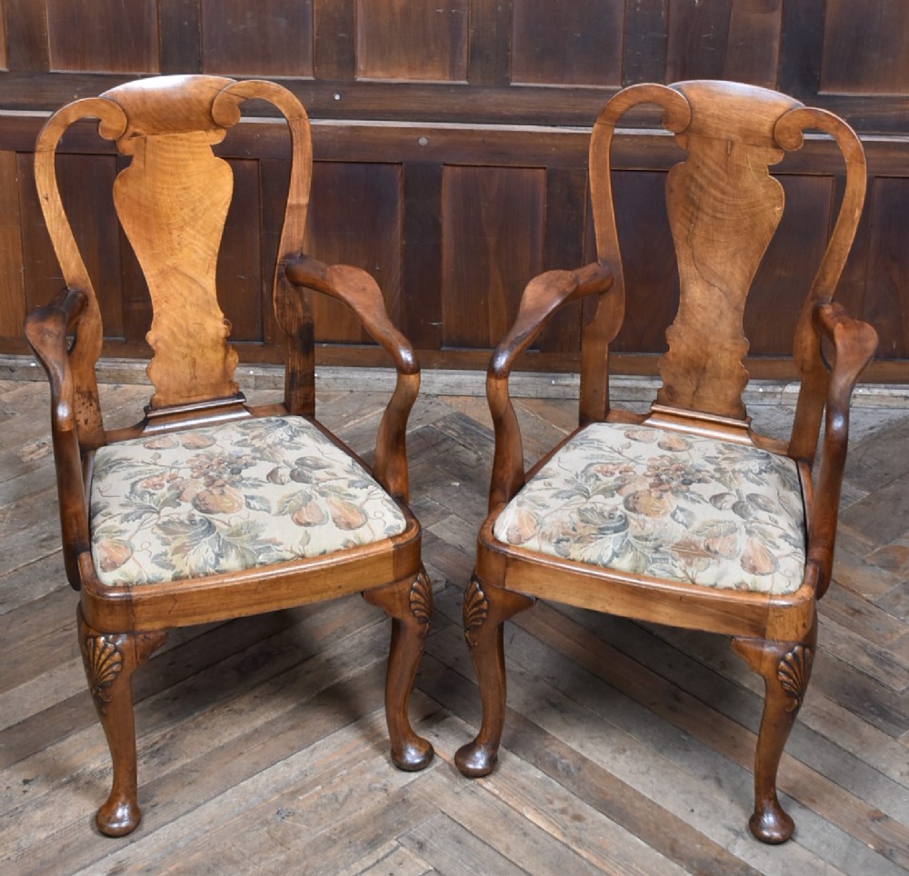 A pair of Victorian Queen Anne style walnut armchairs featuring vase-shaped back splats, carved cabriole legs, and floral patterned drop-in seats.