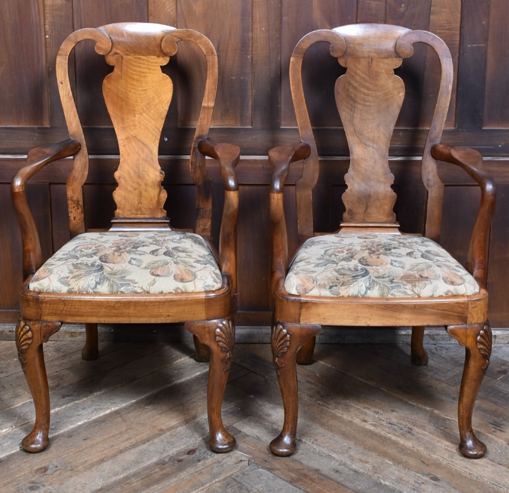 A pair of Victorian Queen Anne style walnut armchairs featuring vase-shaped back splats, carved cabriole legs, and floral patterned drop-in seats. View VI