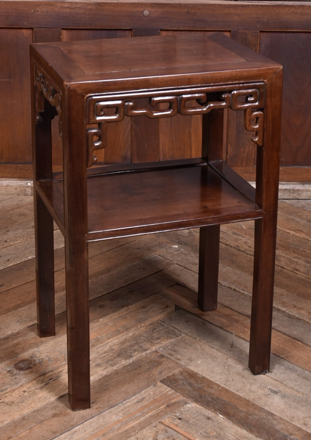 A dark hardwood Chinese vase table featuring a square top, carved fretwork apron, open lower shelf, and straight square legs.