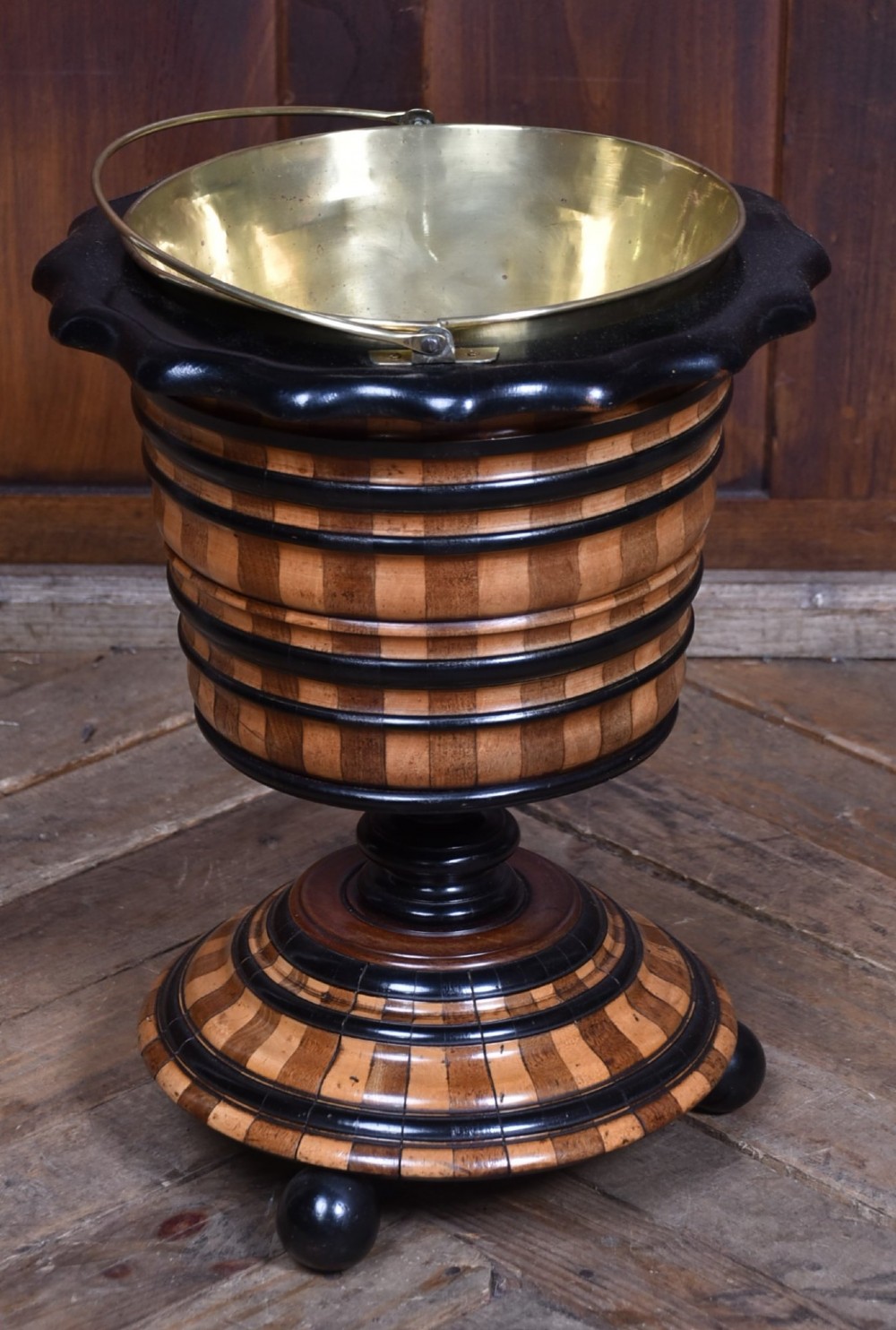 A 19th-century Dutch wooden teestoof featuring alternating light and dark wood parquetry, ebonised trim, turned pedestal base on ball feet, and a removable brass liner with a swing handle. View IV