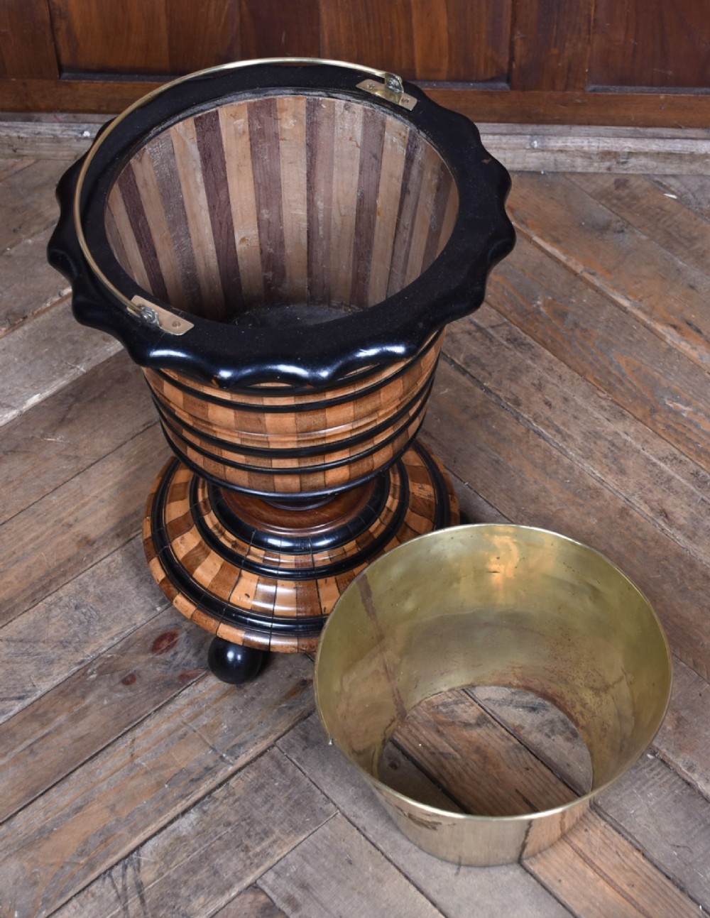 A 19th-century Dutch wooden teestoof featuring alternating light and dark wood parquetry, ebonised trim, turned pedestal base on ball feet, and a removable brass liner with a swing handle. View VI
