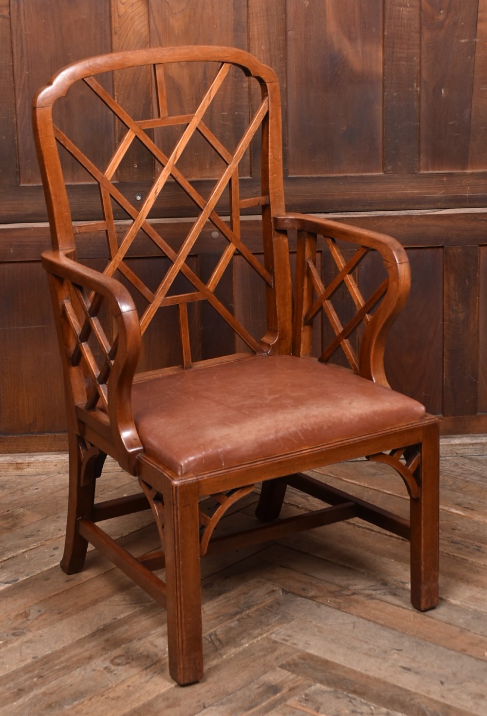 A 19th-century mahogany cockpen armchair featuring geometric lattice fretwork on the backrest and arms, complete with a brown leather drop-in seat.