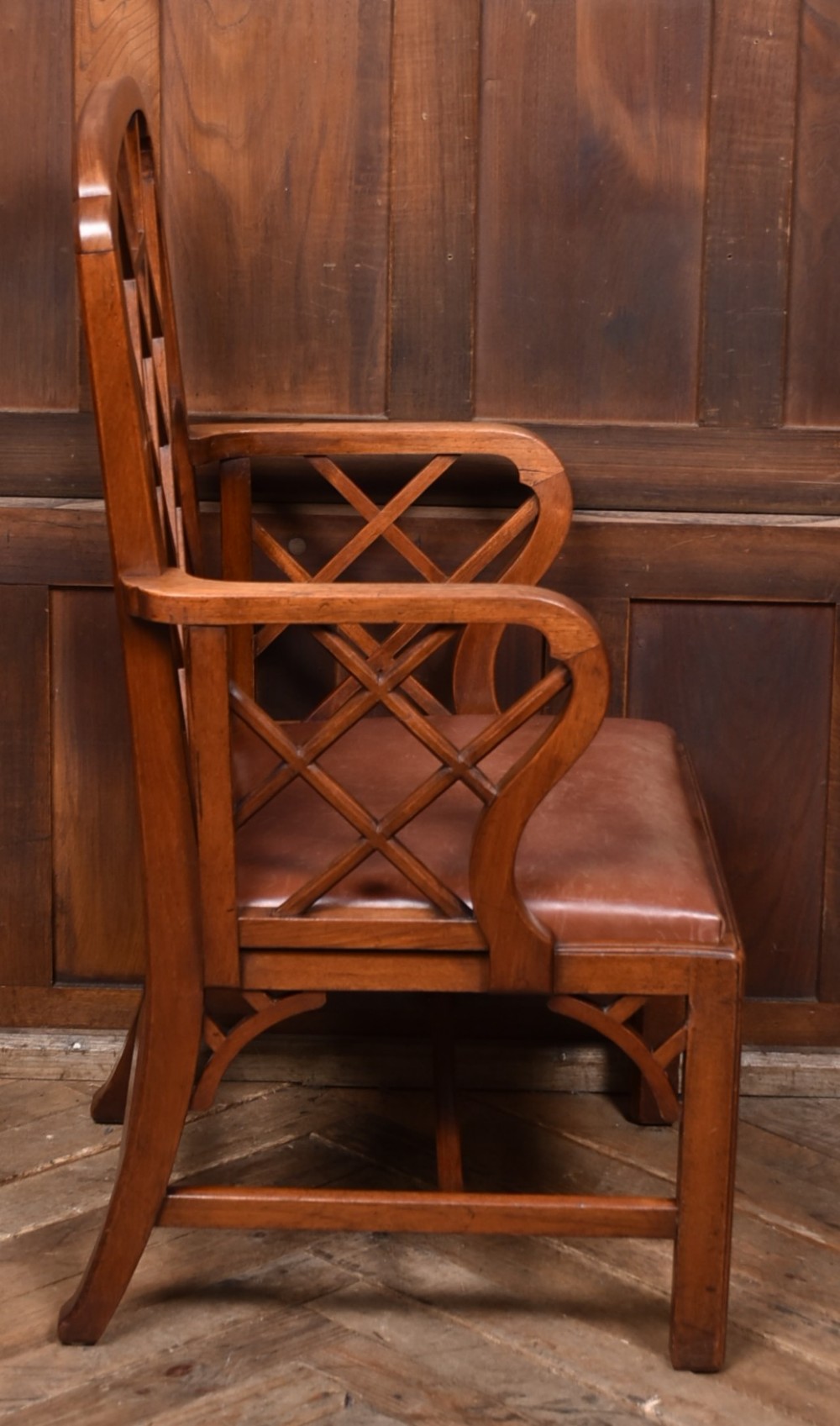 A 19th-century mahogany cockpen armchair featuring geometric lattice fretwork on the backrest and arms, complete with a brown leather drop-in seat. View V