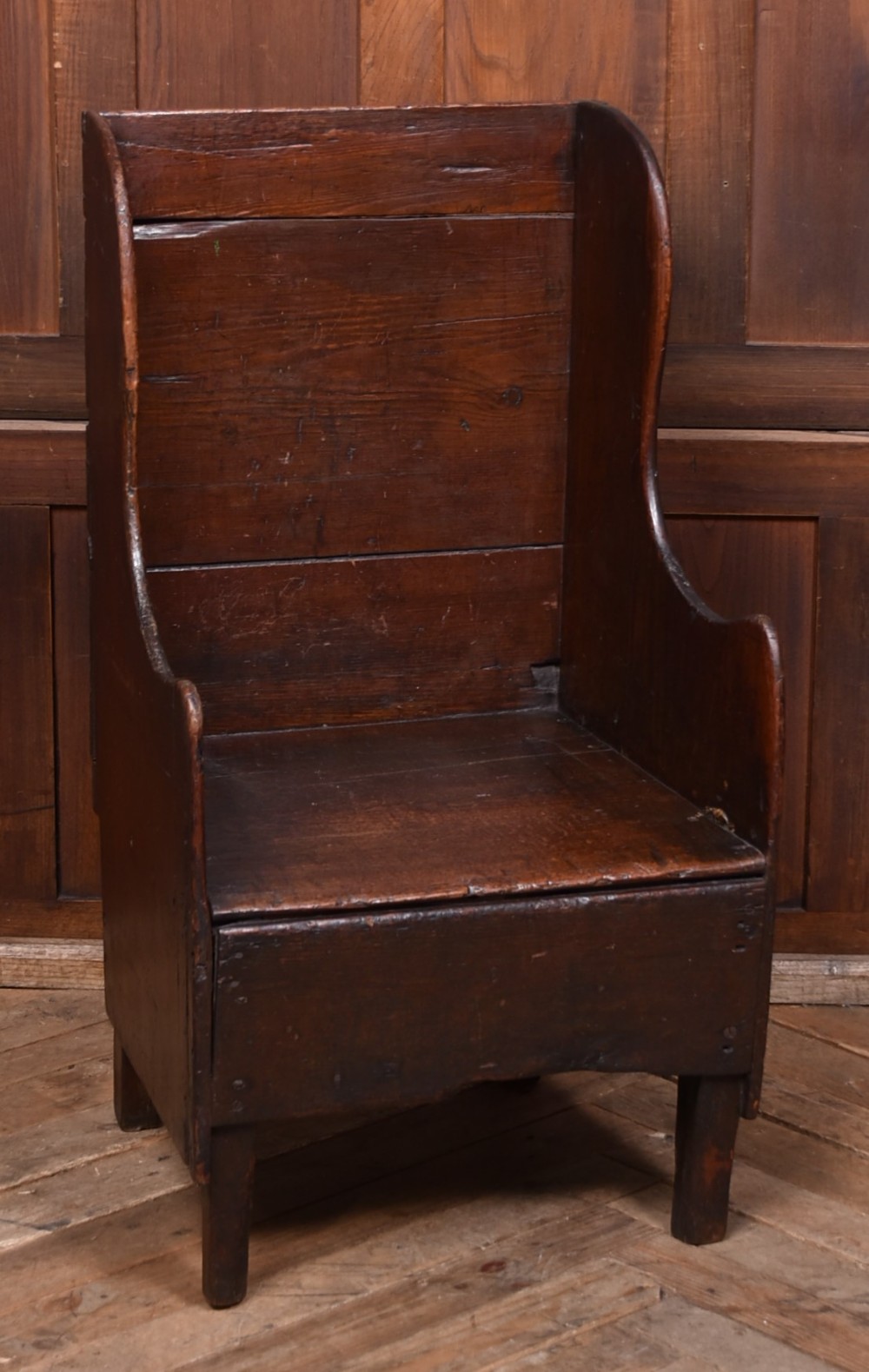 A 19th-century childs lambing chair crafted from dark oak, featuring high solid wings, a panelled backrest, an enclosed box seat, and short square legs.