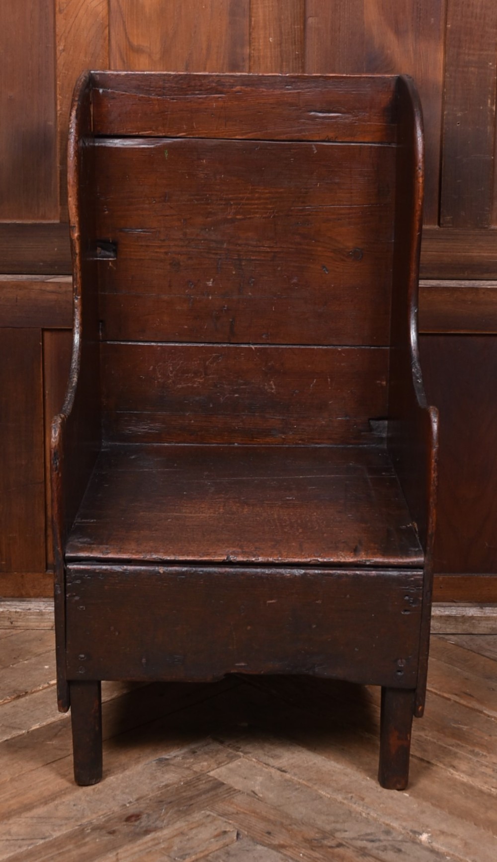 A 19th-century childs lambing chair crafted from dark oak, featuring high solid wings, a panelled backrest, an enclosed box seat, and short square legs. View II