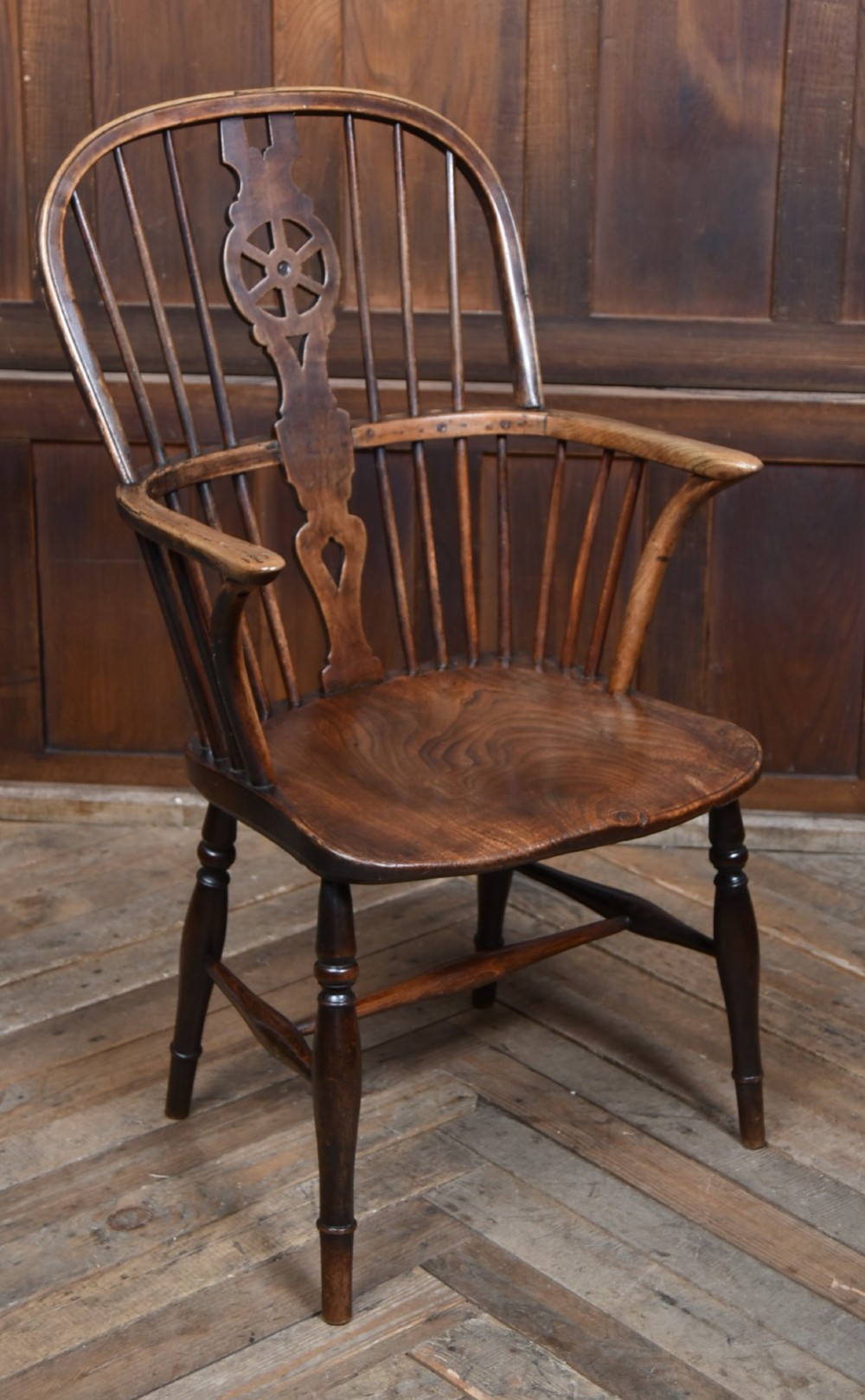 A 19th-century dark wood Windsor armchair featuring a pierced wheel back splat, spindle backrest, curved armrests, shaped seat, and turned legs.