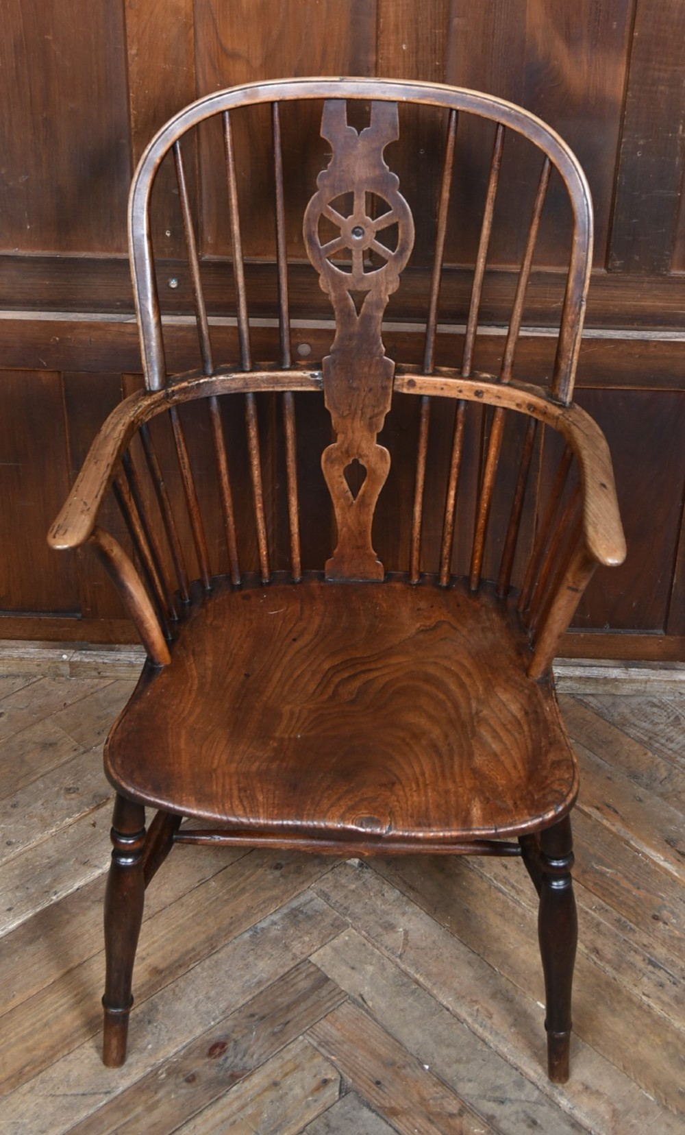 A 19th-century dark wood Windsor armchair featuring a pierced wheel back splat, spindle backrest, curved armrests, shaped seat, and turned legs. View V