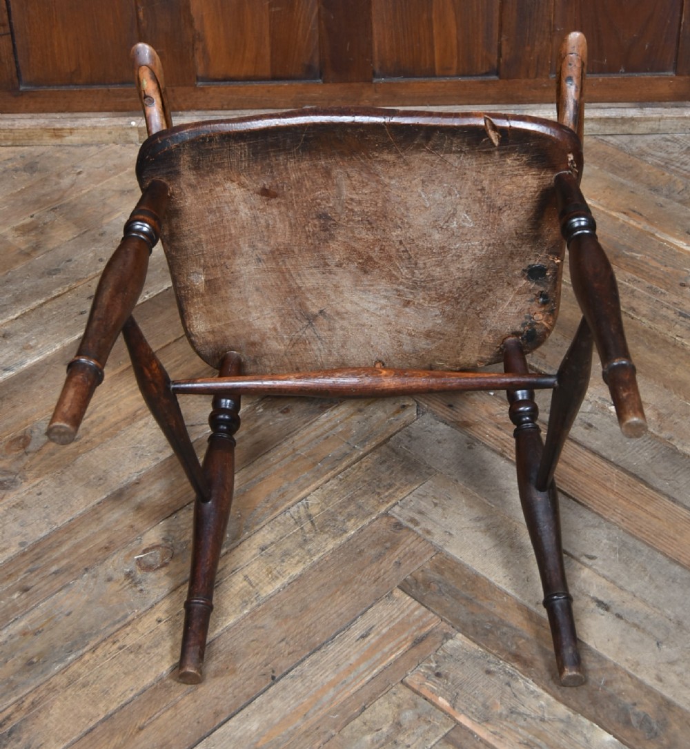 A 19th-century dark wood Windsor armchair featuring a pierced wheel back splat, spindle backrest, curved armrests, shaped seat, and turned legs. View X