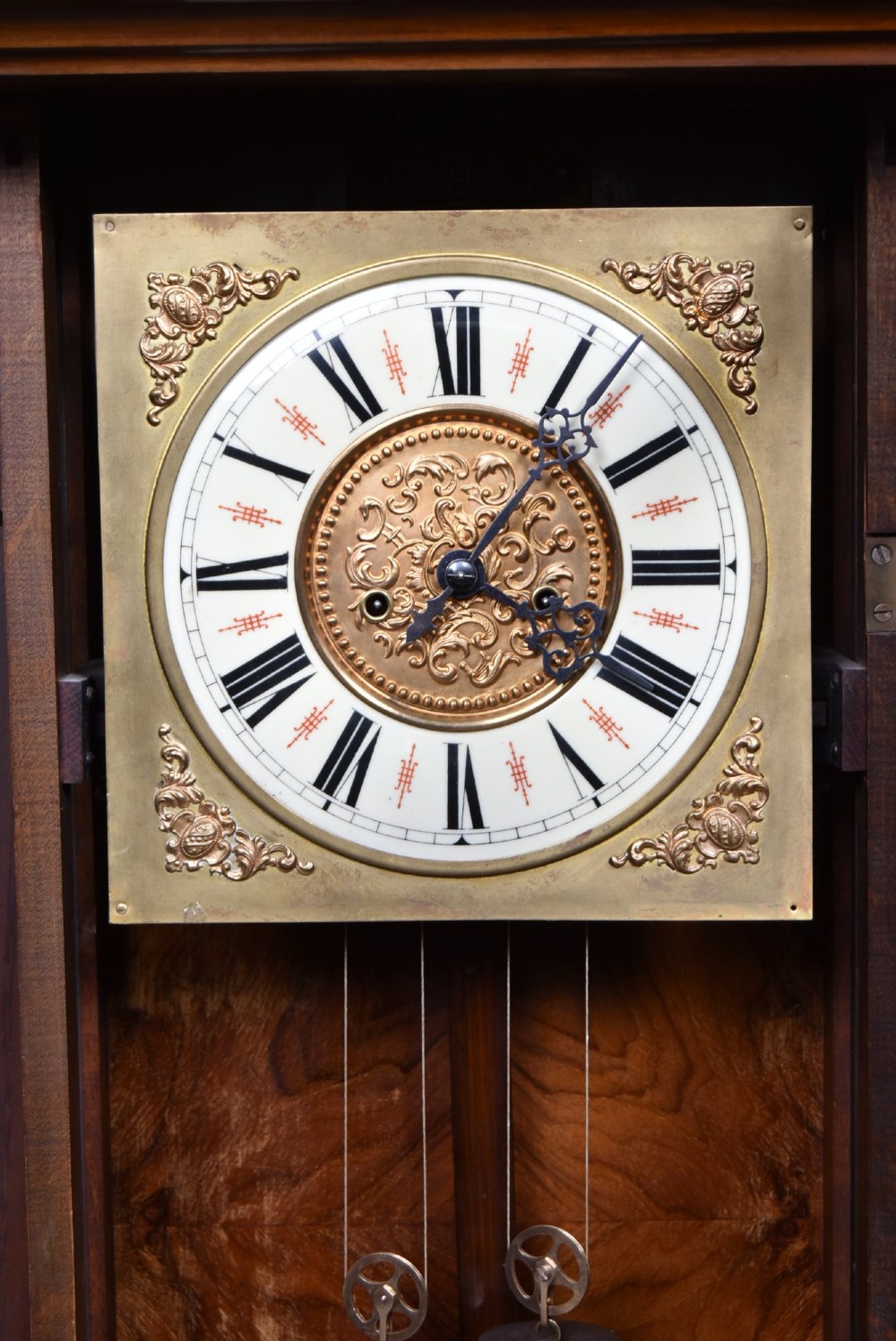 A late 19th-century Vienna-style wall clock featuring a dark walnut carved wood case, turned side columns, decorative pediment, brass weights, and a brass pendulum. View VII