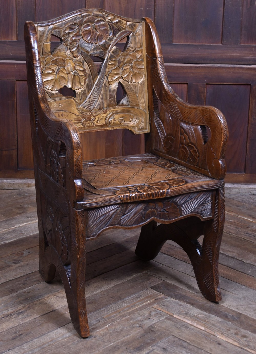An antique carved walnut armchair featuring intricate floral relief carvings on the backrest, armrests, and legs.