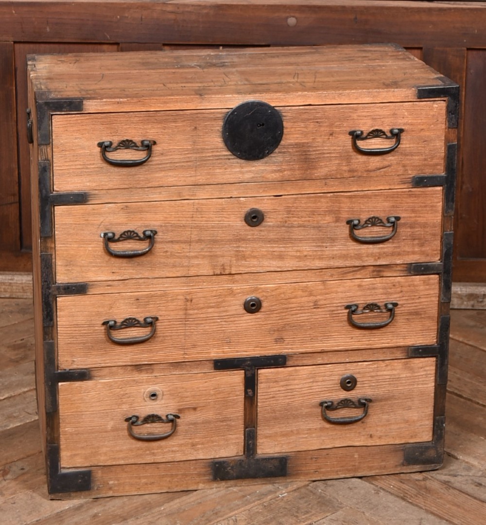 A traditional wooden Japanese tansu chest featuring four tiers of drawers accented with dark iron handles and corner brackets.