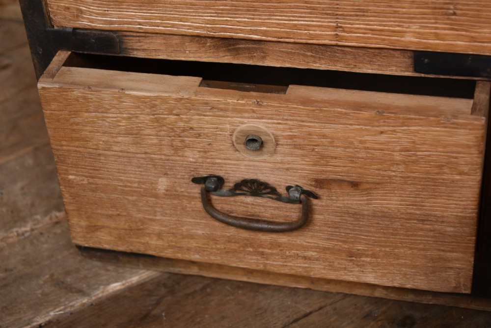 A traditional wooden Japanese tansu chest featuring four tiers of drawers accented with dark iron handles and corner brackets. View V