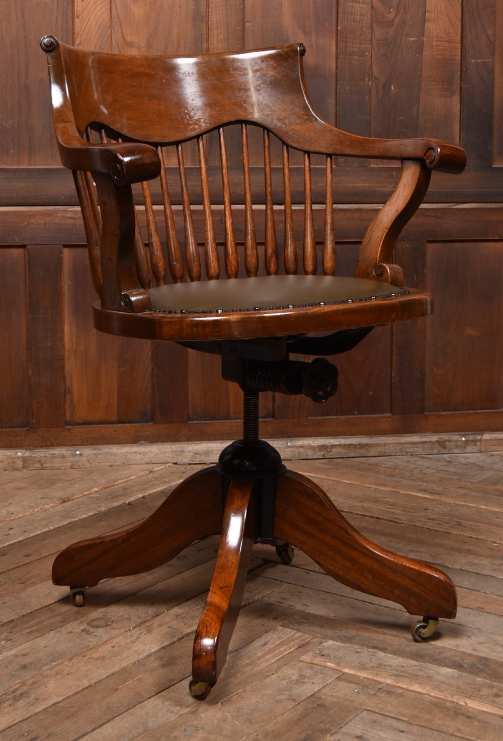 An Edwardian carved mahogany swivel desk chair featuring a spindle backrest, dark leather upholstered seat with studding detail, and a quadruped base on brass castors. View II