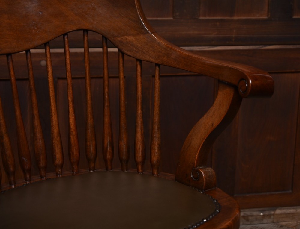 An Edwardian carved mahogany swivel desk chair featuring a spindle backrest, dark leather upholstered seat with studding detail, and a quadruped base on brass castors. View III