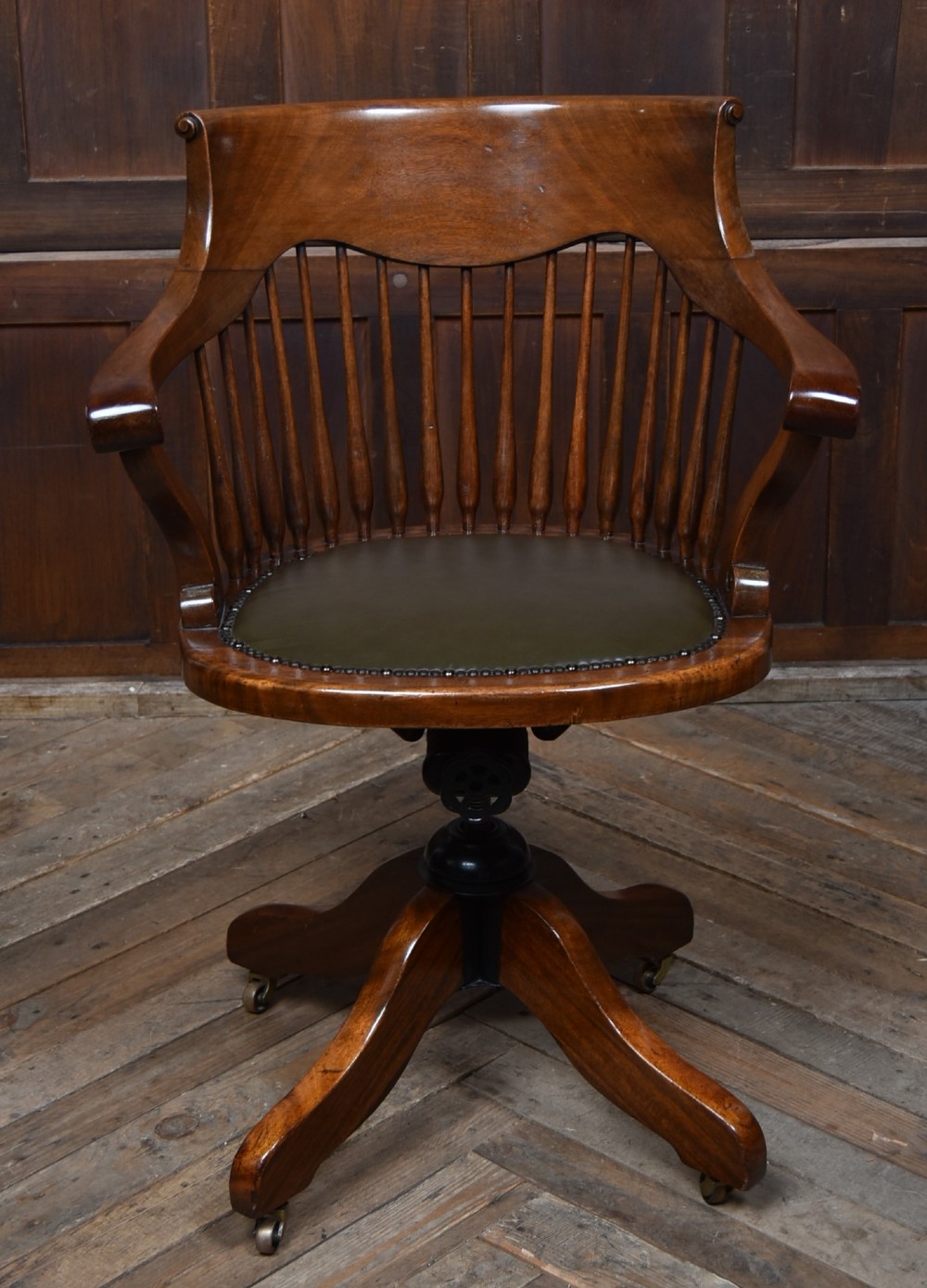 An Edwardian carved mahogany swivel desk chair featuring a spindle backrest, dark leather upholstered seat with studding detail, and a quadruped base on brass castors. View IV