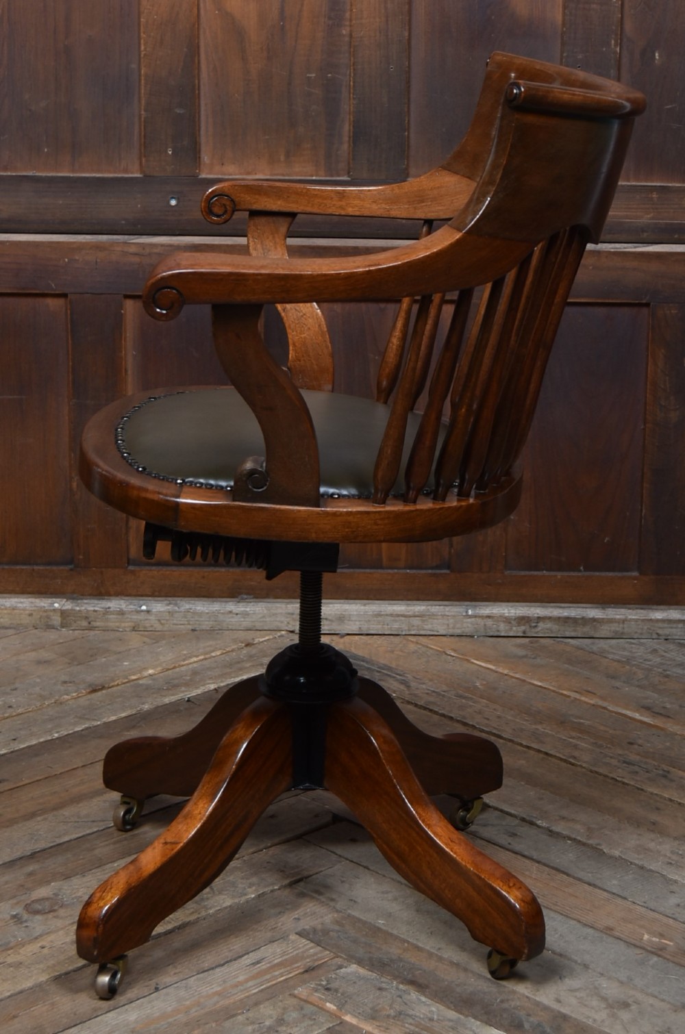An Edwardian carved mahogany swivel desk chair featuring a spindle backrest, dark leather upholstered seat with studding detail, and a quadruped base on brass castors. View VIII