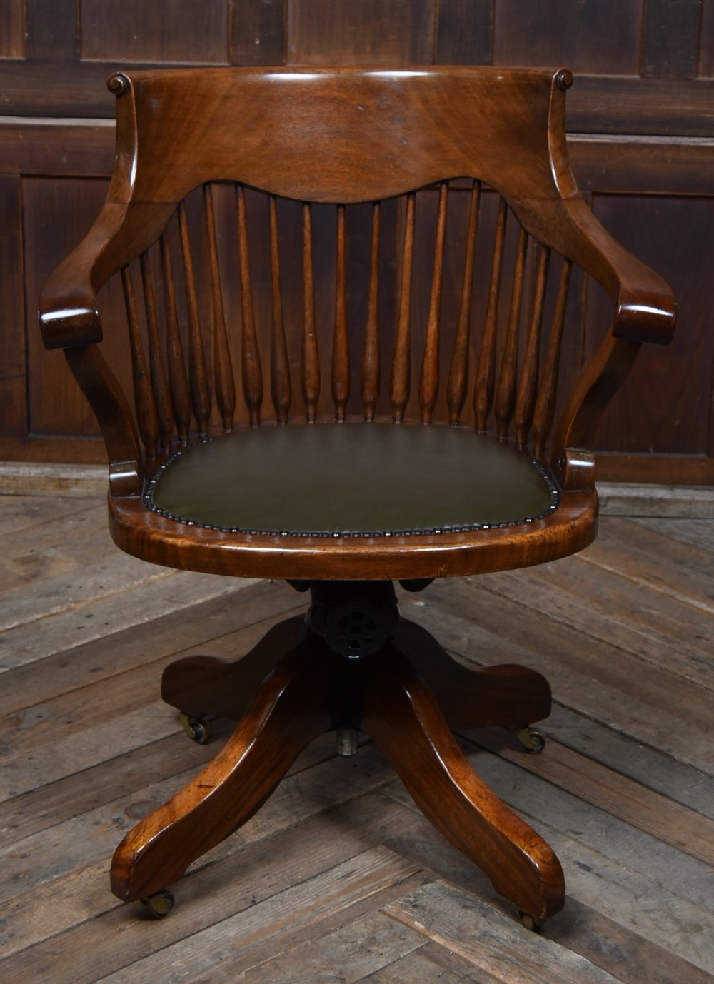 An Edwardian carved mahogany swivel desk chair featuring a spindle backrest, dark leather upholstered seat with studding detail, and a quadruped base on brass castors. View IX
