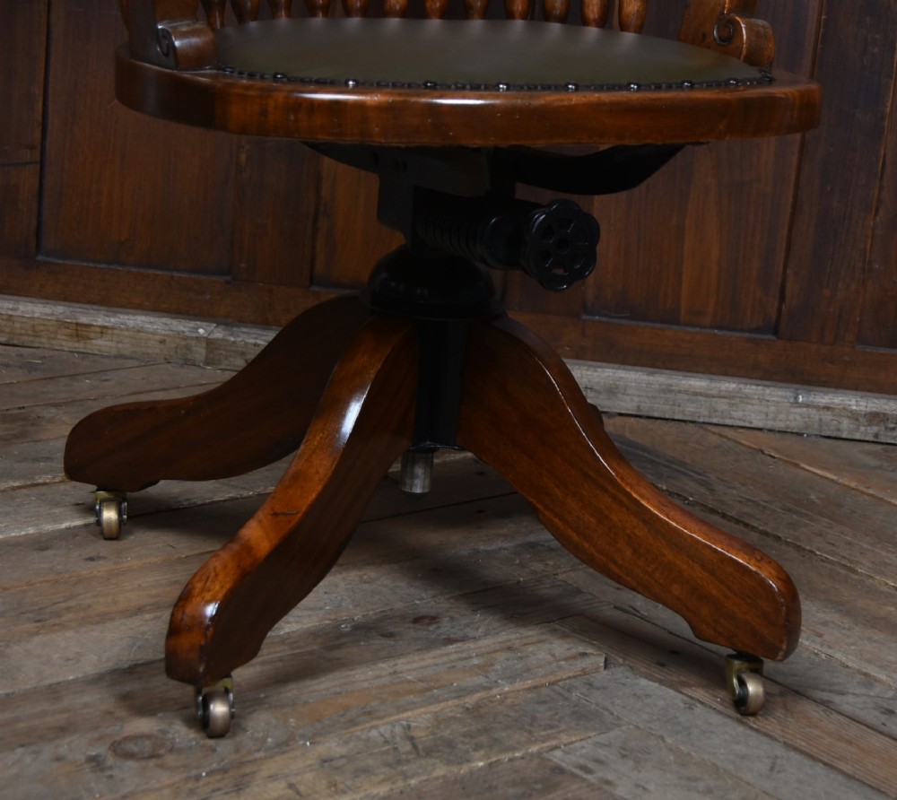 An Edwardian carved mahogany swivel desk chair featuring a spindle backrest, dark leather upholstered seat with studding detail, and a quadruped base on brass castors. View X