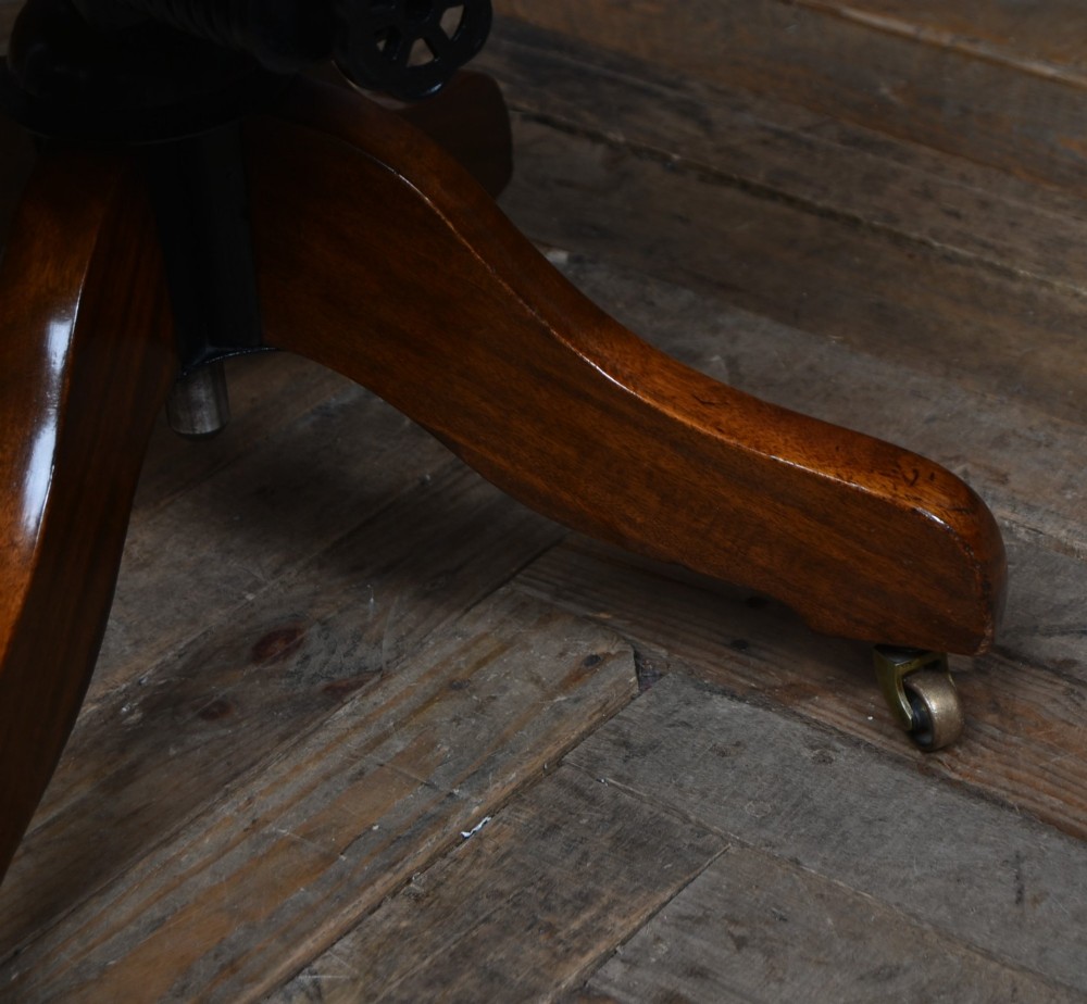 An Edwardian carved mahogany swivel desk chair featuring a spindle backrest, dark leather upholstered seat with studding detail, and a quadruped base on brass castors. View XI