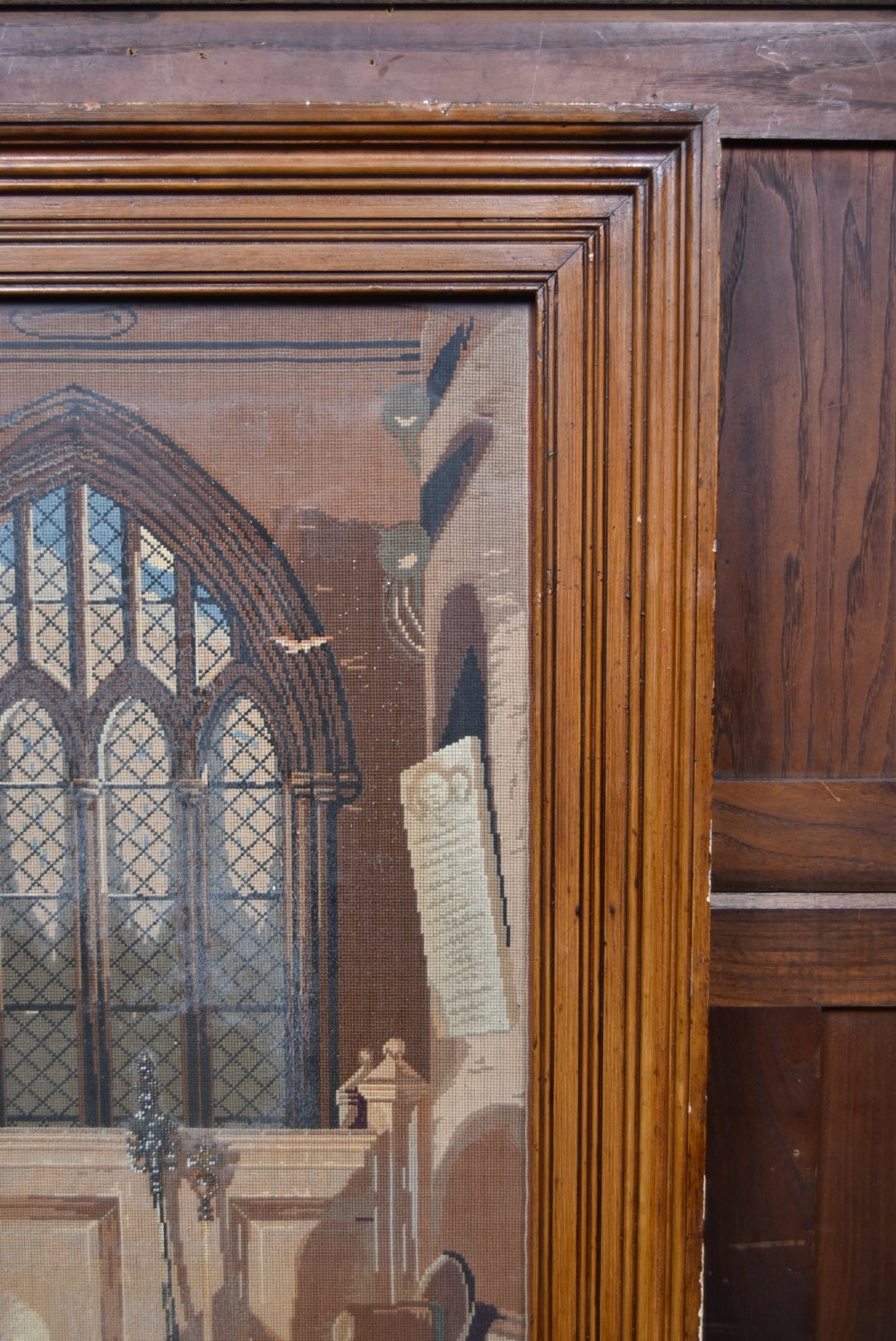 A framed needlepoint tapestry depicting figures and a crown inside an ecclesiastical interior with light streaming through a Gothic window. View IV