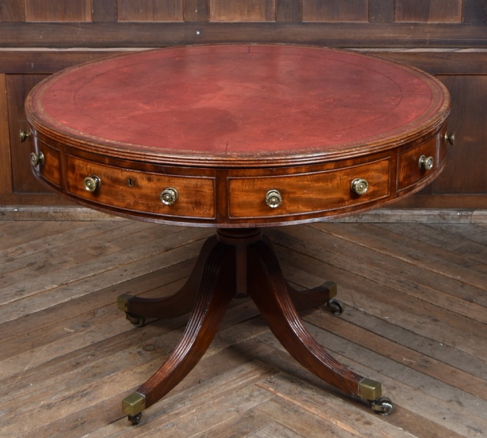 A circular Georgian mahogany drum table featuring a red leather inset top, frieze drawers with brass knobs, and a central pedestal with reeded splayed legs.