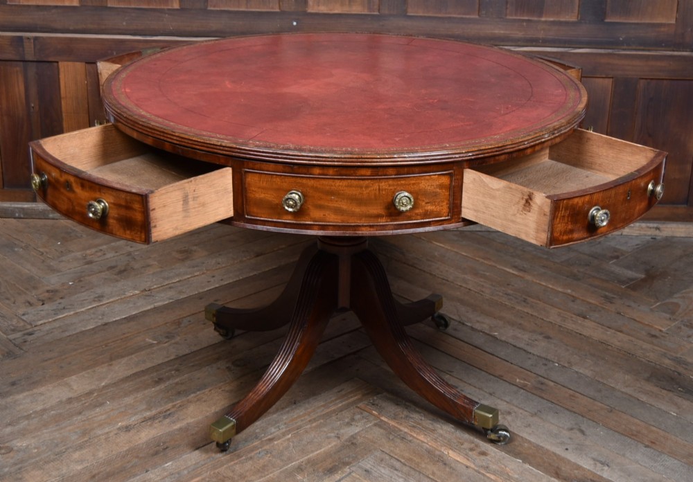 A circular Georgian mahogany drum table featuring a red leather inset top, frieze drawers with brass knobs, and a central pedestal with reeded splayed legs. View VI