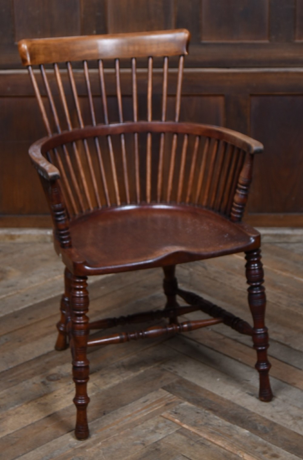An Edwardian wooden comb-back Windsor armchair with turned legs, spindle backrest, and a contoured saddle seat.