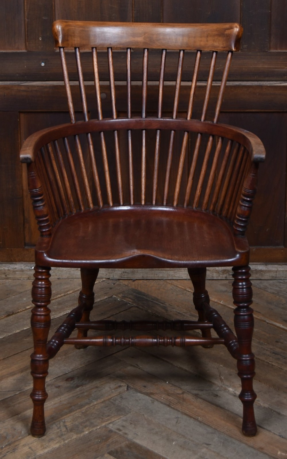 An Edwardian wooden comb-back Windsor armchair with turned legs, spindle backrest, and a contoured saddle seat. View V