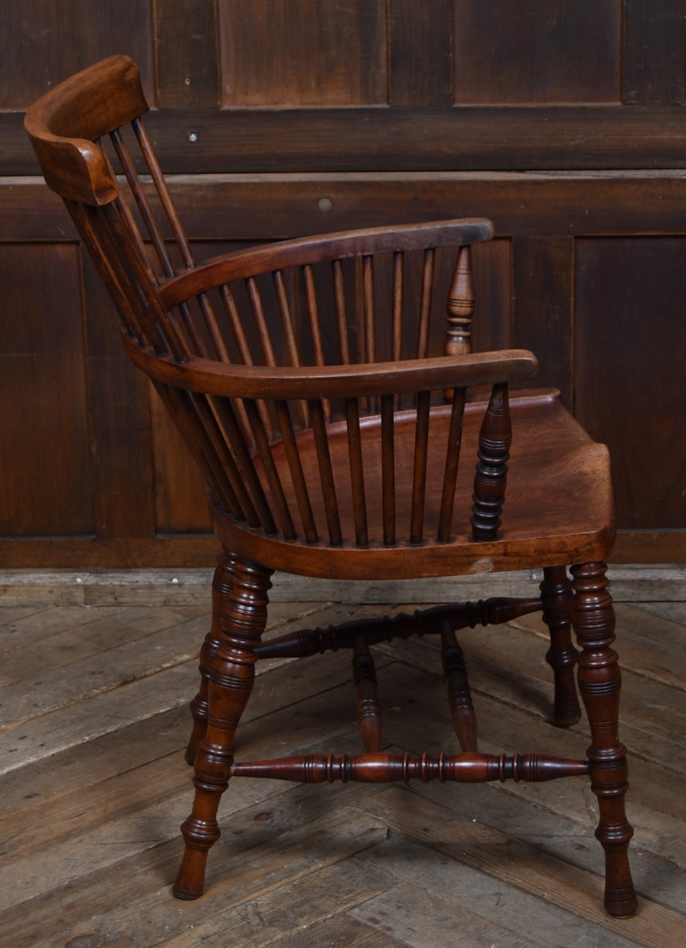 An Edwardian wooden comb-back Windsor armchair with turned legs, spindle backrest, and a contoured saddle seat. View VI