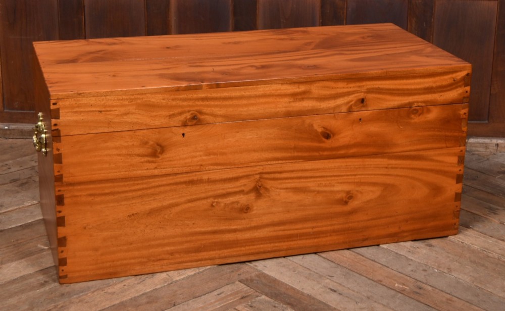 A rectangular warm amber camphor wood blanket box featuring exposed dovetail corner joints and metal side handles.