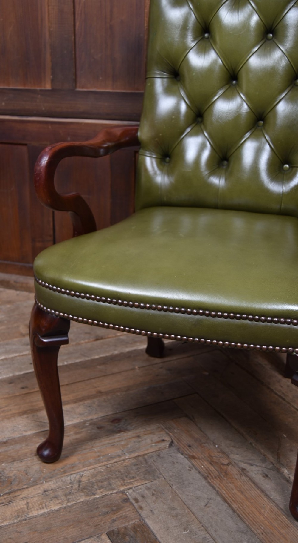 A high-backed desk chair featuring olive green button-tufted leather upholstery, carved dark wood armrests, brass stud trimming, and front cabriole legs. View III
